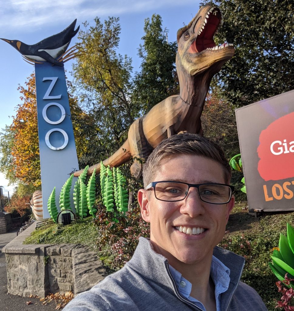 A man takes a selfie in front of a zoo sign.