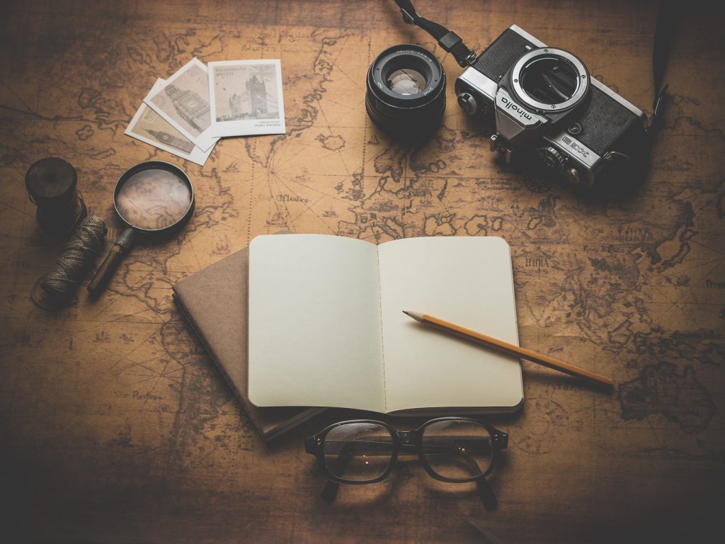 A notebook, camera, magnifying glass and map on a wooden table.
